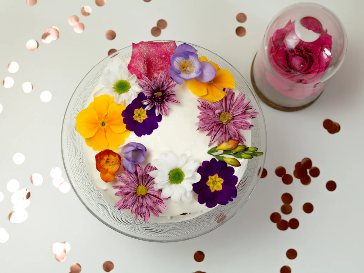 Spritzbeutel mit Sterntülle, Palette, Drehteller und Schälchen mit essbaren Blüten auf einer Küchenarbeitsplatte