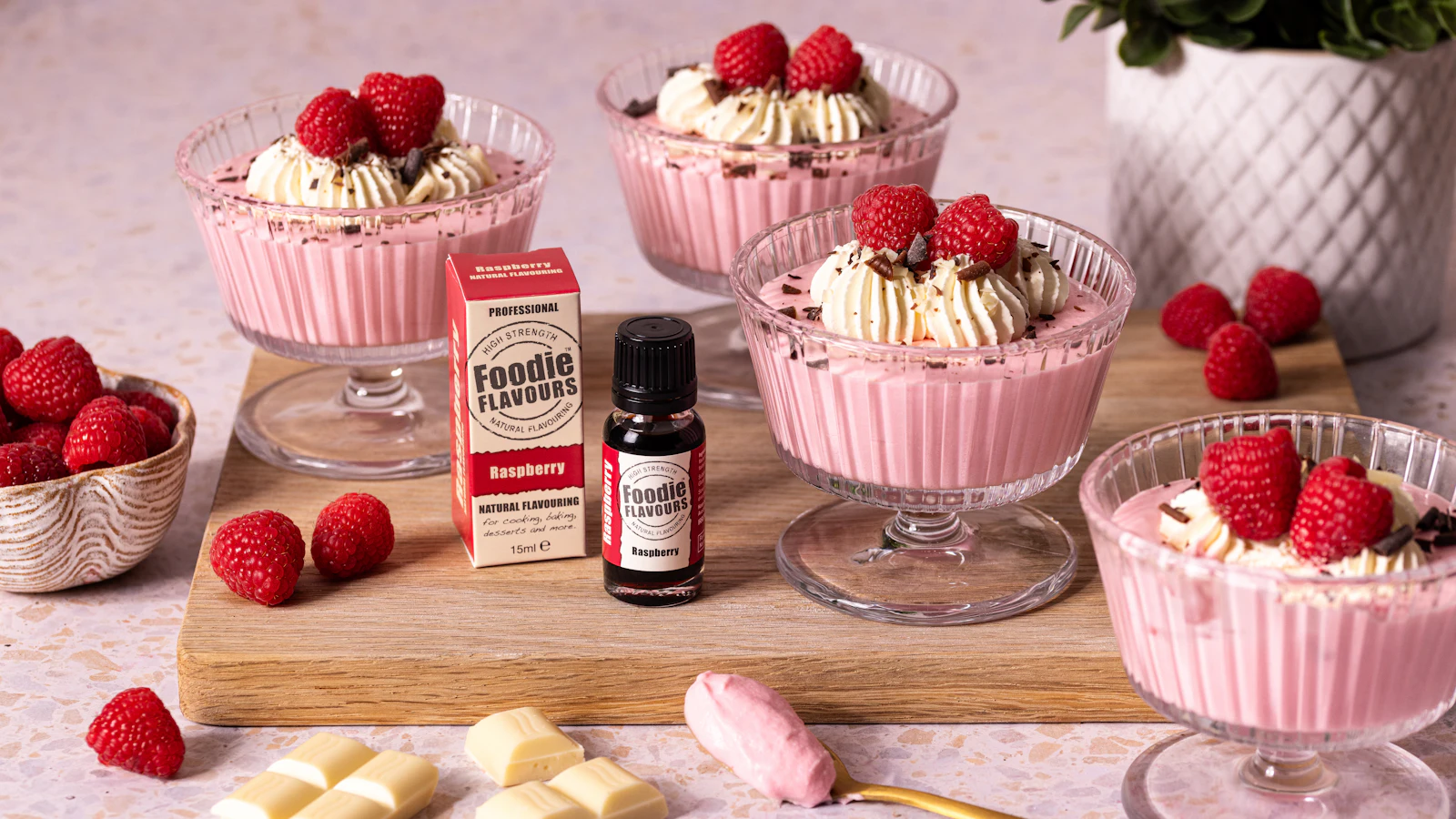 Tassenkuchen mit geschmolzenem Schokoladenkern in einer weißen Tasse, daneben zwei Gläser mit Quarkcreme und frischen Himbeeren