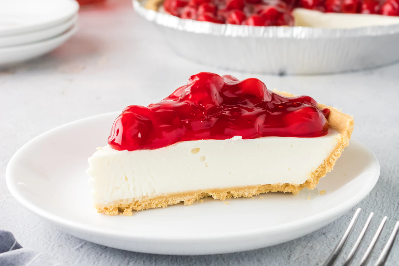 No-Bake-Cheesecake mit Keksboden und Himbeeren auf einer Tortenplatte, daneben Gläser mit Panna cotta und eine Form Tiramisu